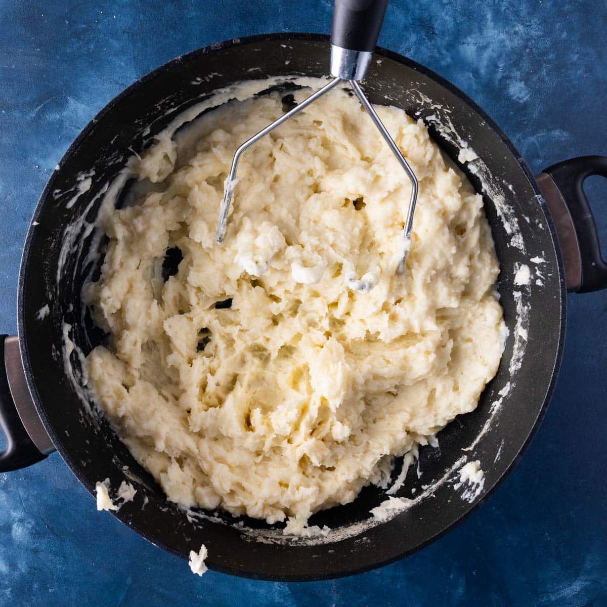 mashed potatoes in a pot with a potato masher