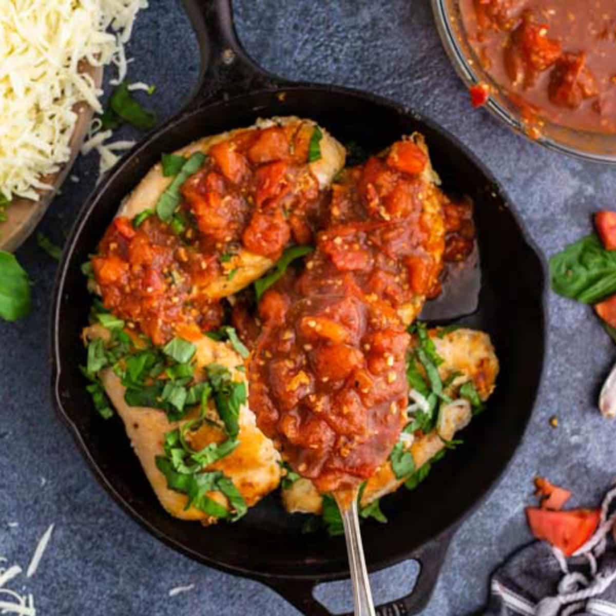 spooning tomato sauce over chicken in a skillet