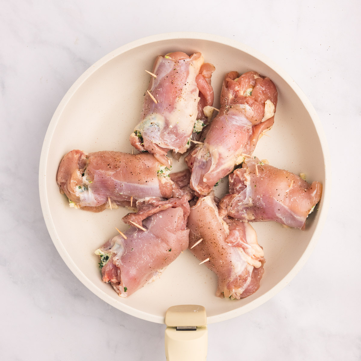 uncooked chicken thighs rolled with cheese in the middle in a skillet