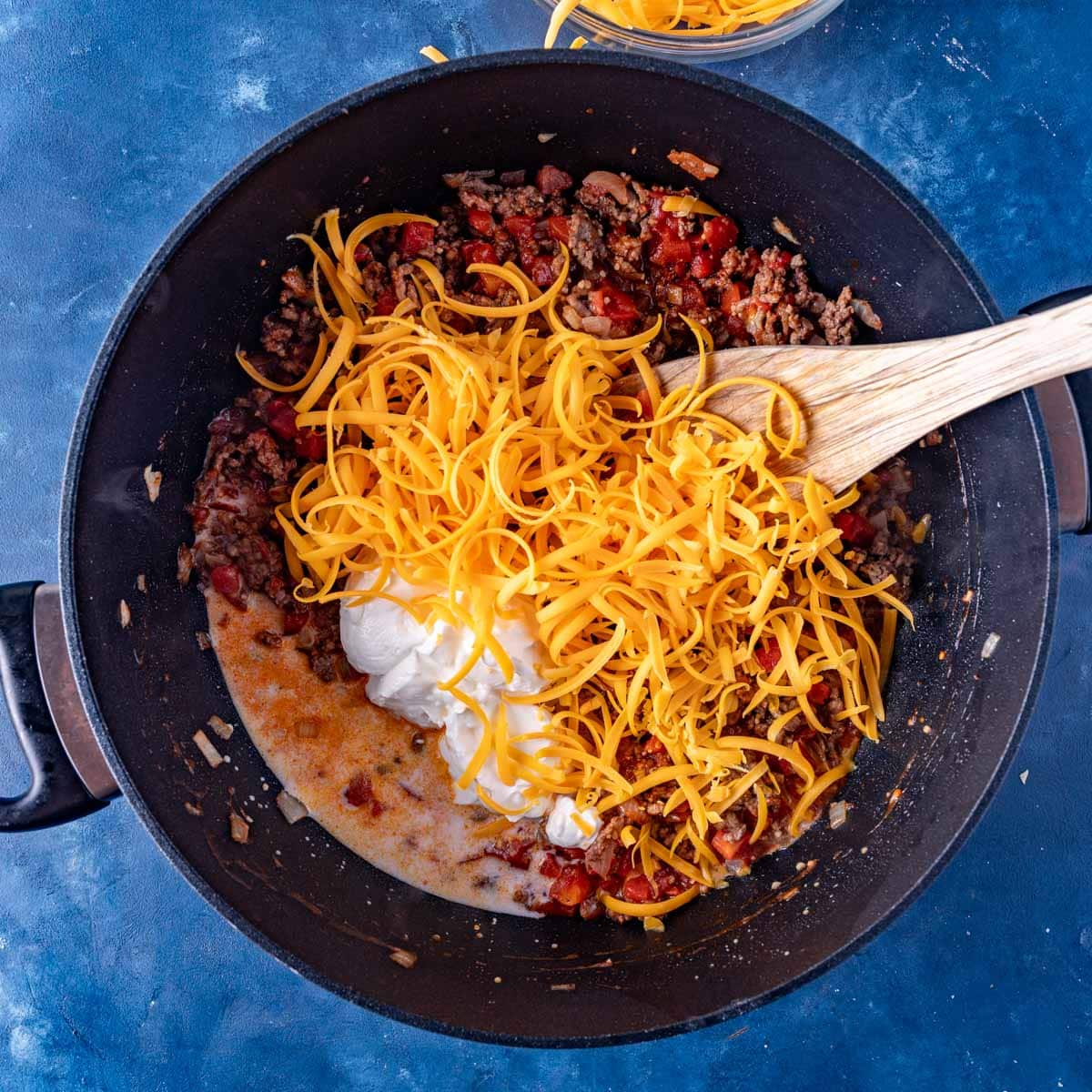 cheese and sour cream over cooked ground beef in a skillet