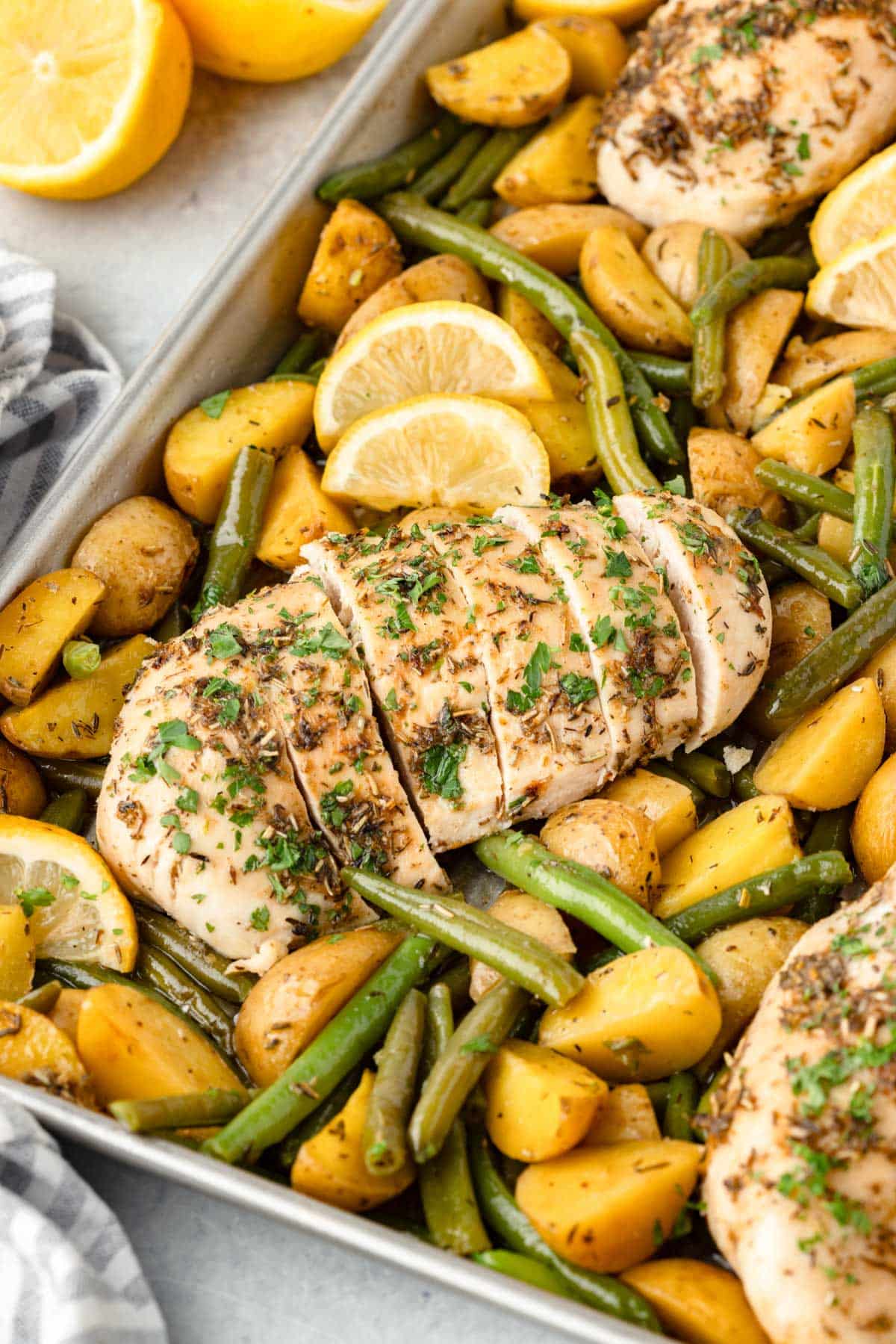 sliced chicken on a sheet pan with potatoes and green beans