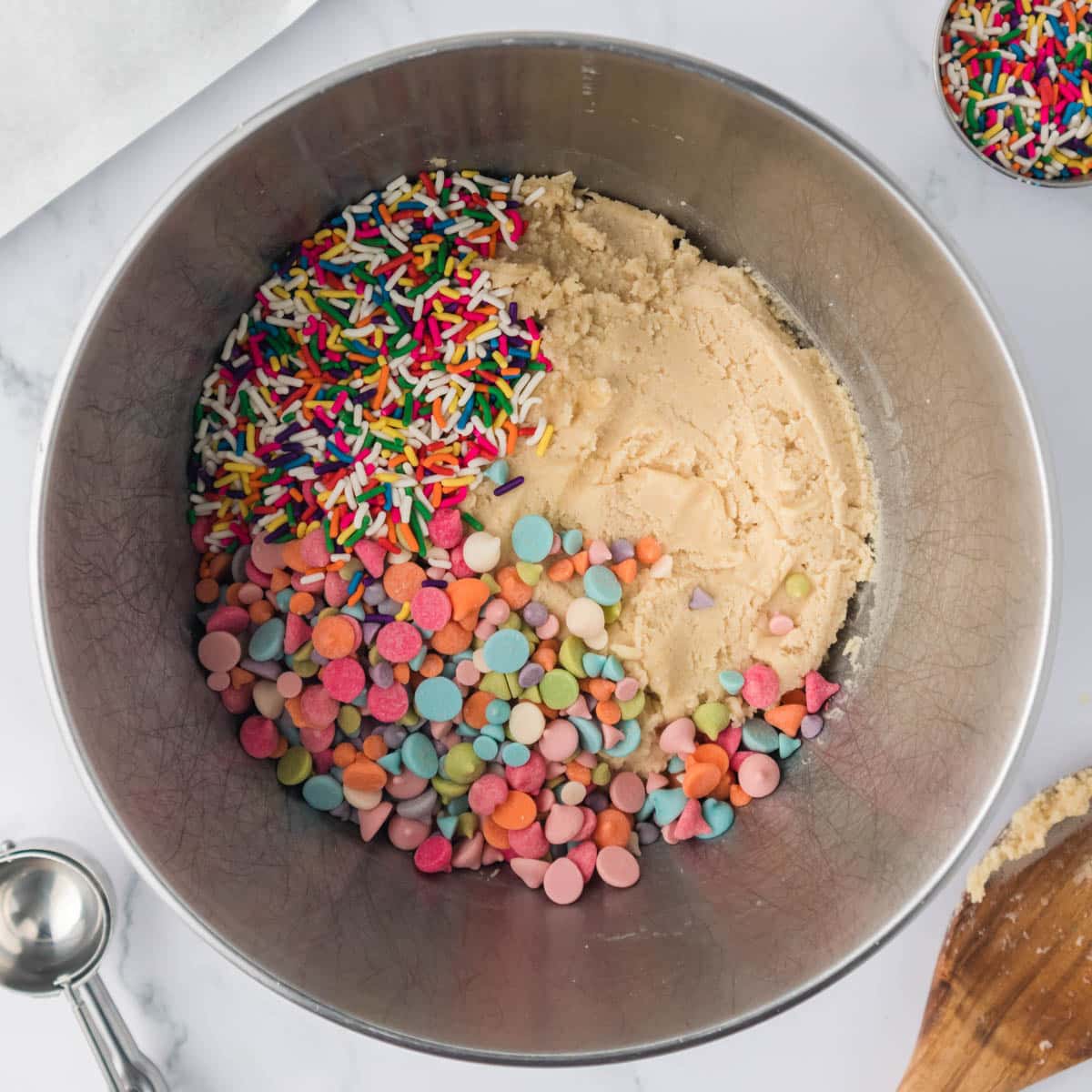 sprinkles and rainbow chips over cookie dough in a bowl