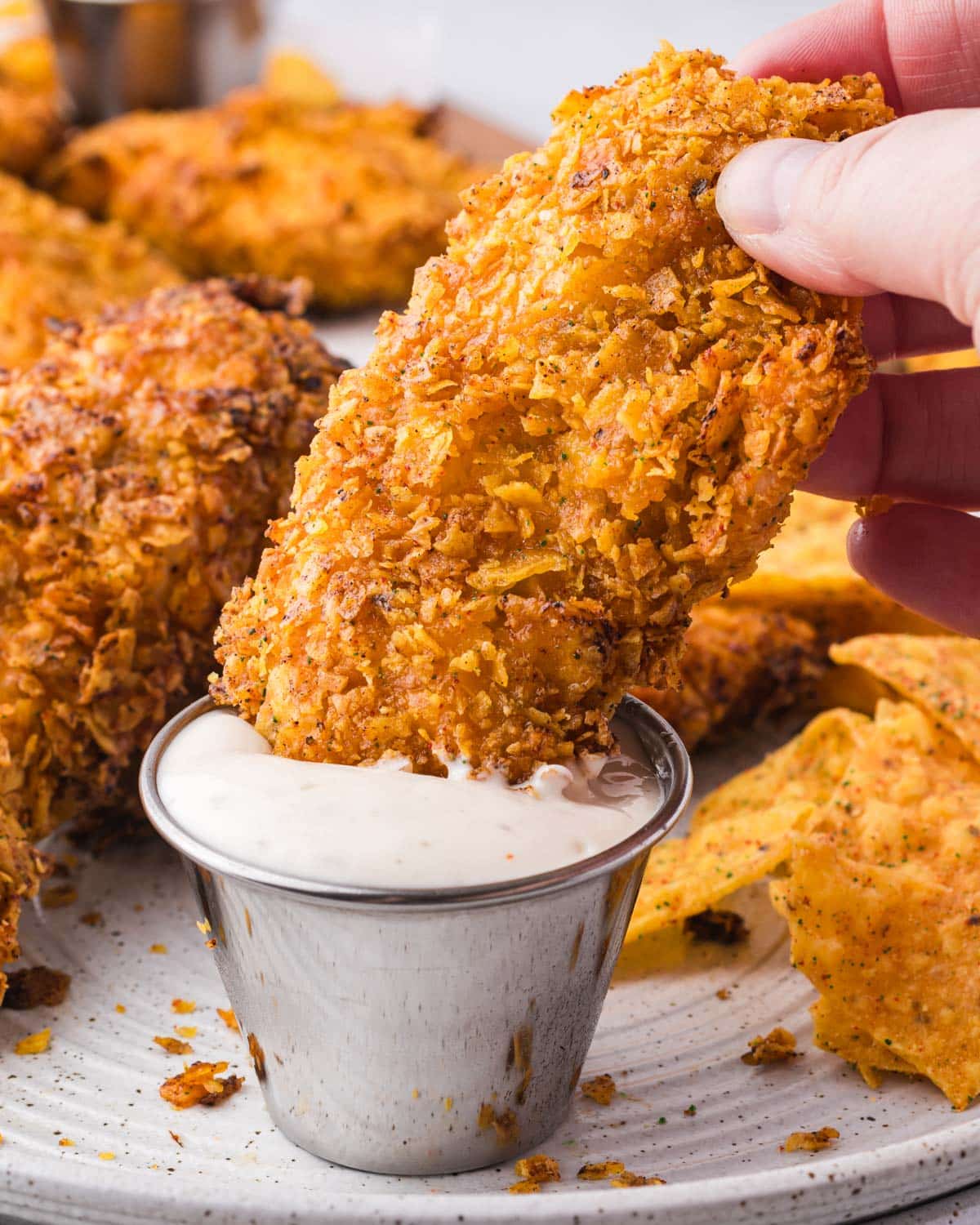 a hand dipping a chicken tender into ranch dip