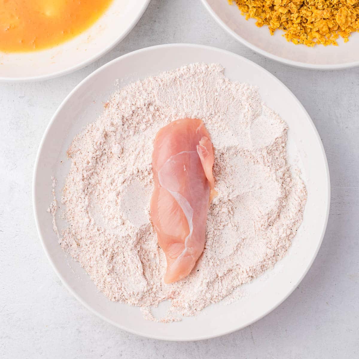 a chicken tender on a plate of seasoned flour