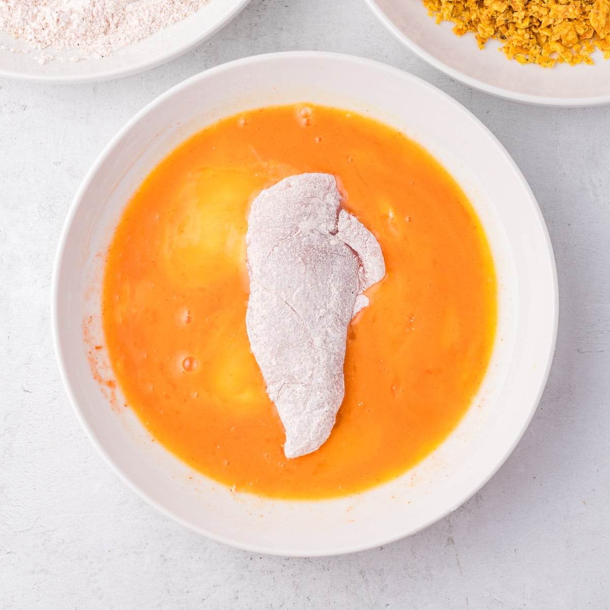 a floured chicken tender in a bowl of beaten eggs