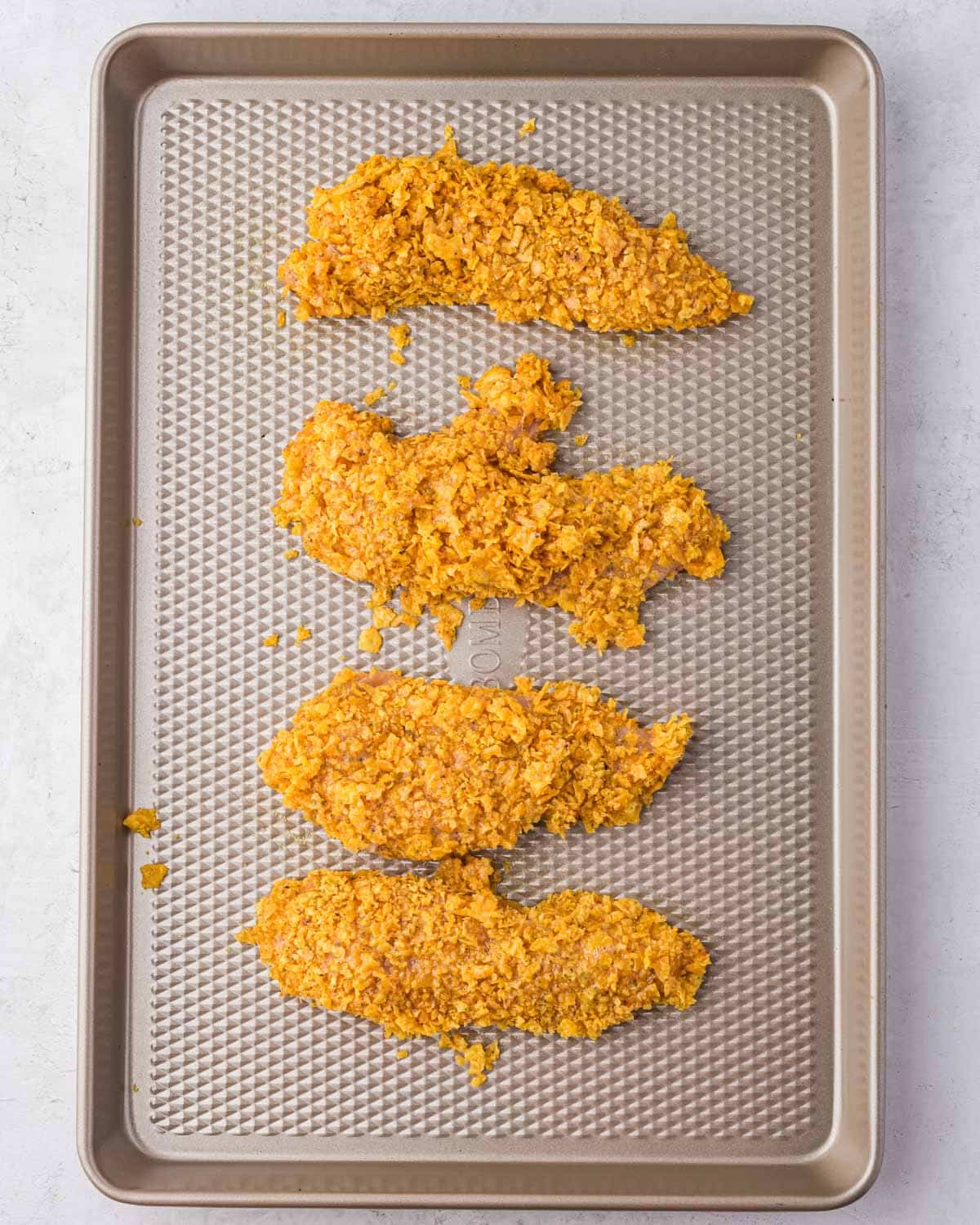 4 chicken tenders coated with crushed doritos on a baking sheet