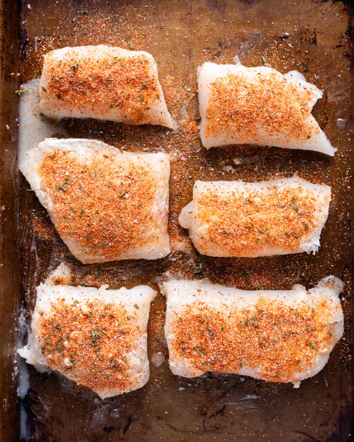 unbaked cod with seasoning on a baking sheet