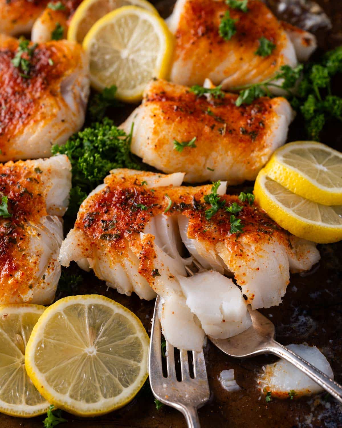 forks cutting into baked cod on a baking sheet