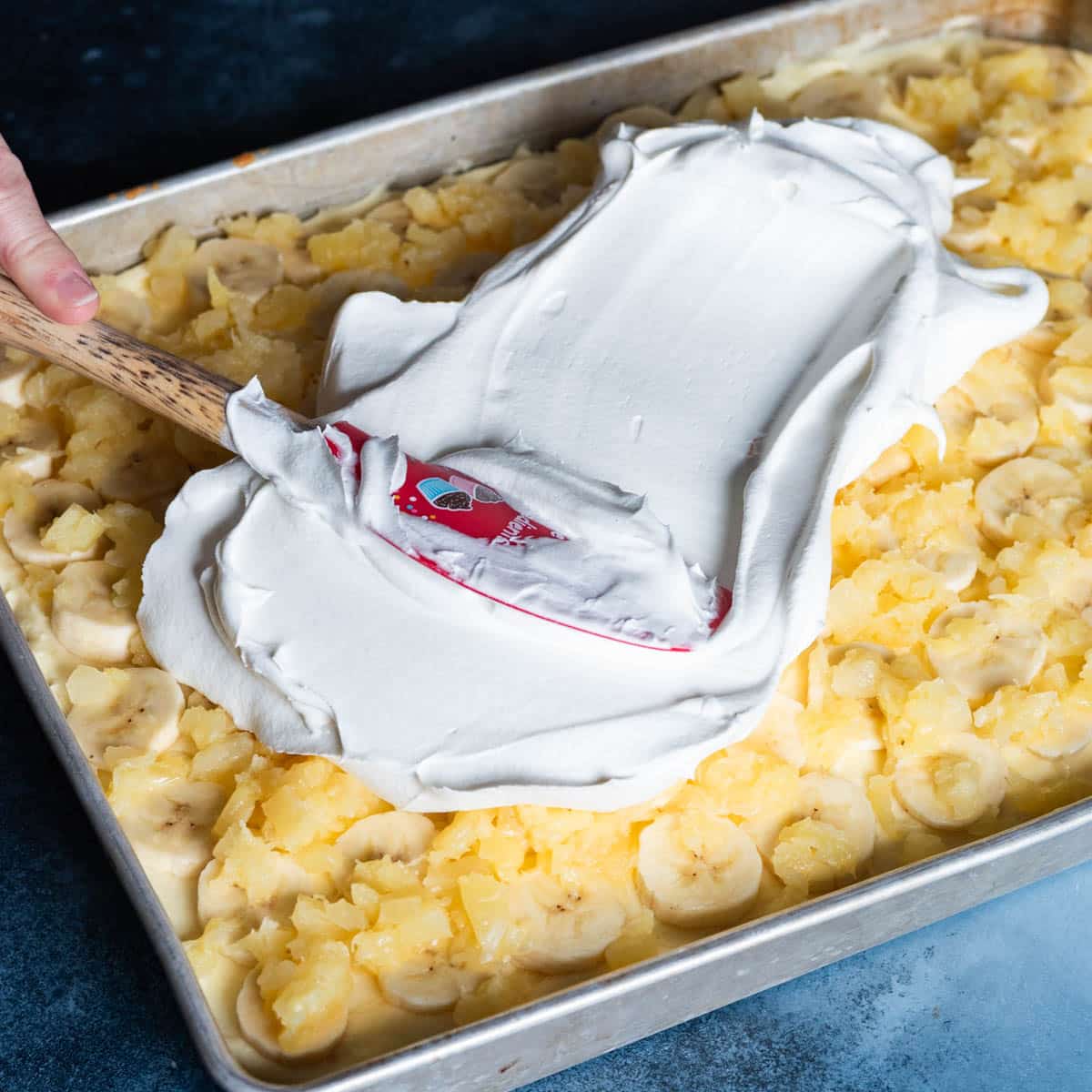 spreading cool whip over a banana and pineapple cake