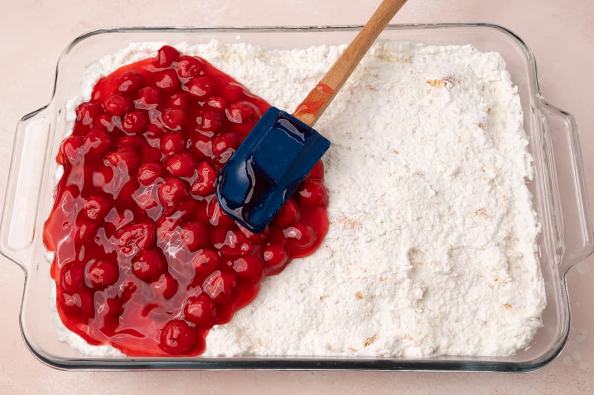 spreading cherry pie filling over angel food cake in a glass pan