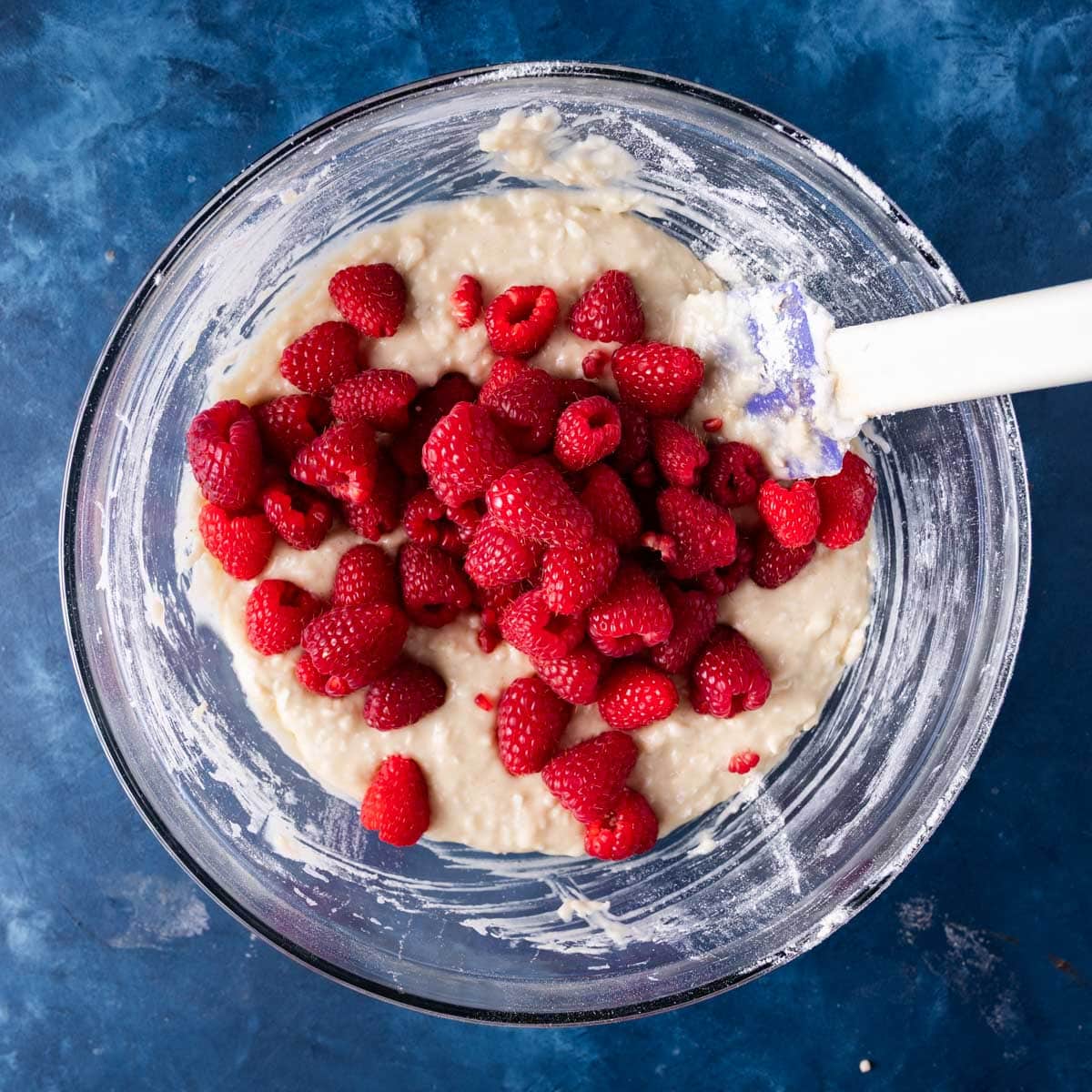 fresh raspberries over muffin batter in a bowl