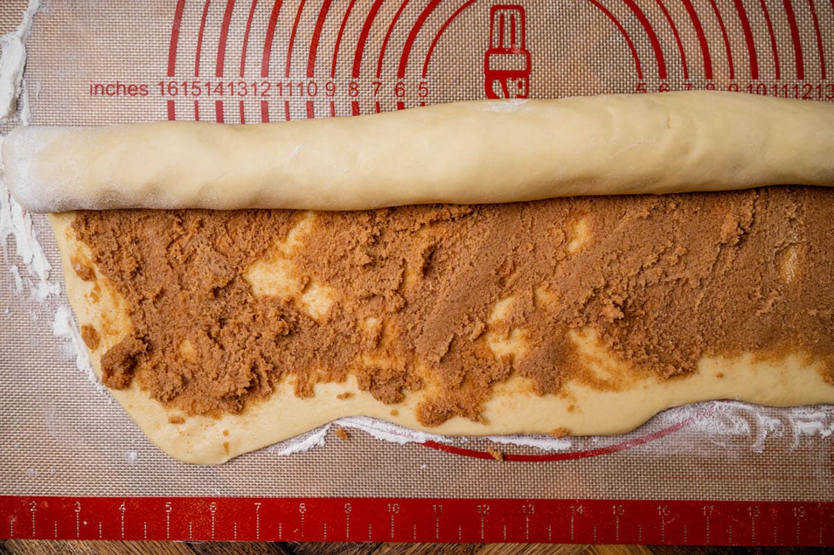 rolled up cinnamon roll dough on a pastry mat